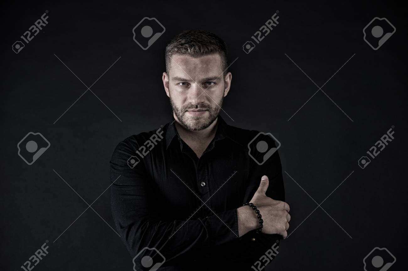 91167093-macho-in-black-shirt-pose-with-folded-hands-man-with-bearded-face-and-stylish-hair-on...jpg